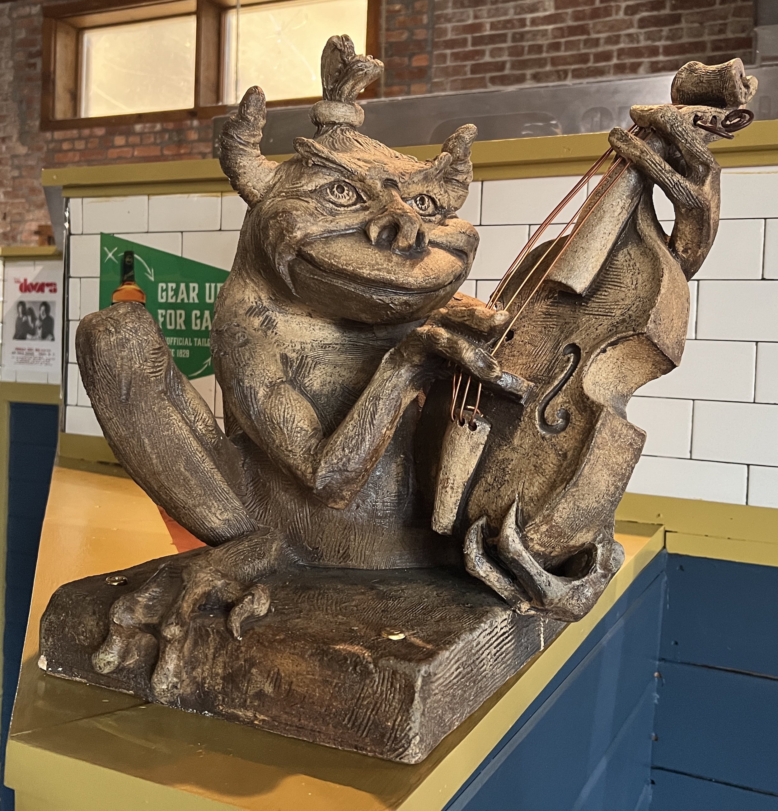 Sculpture of gremlin plucking strings of violin.